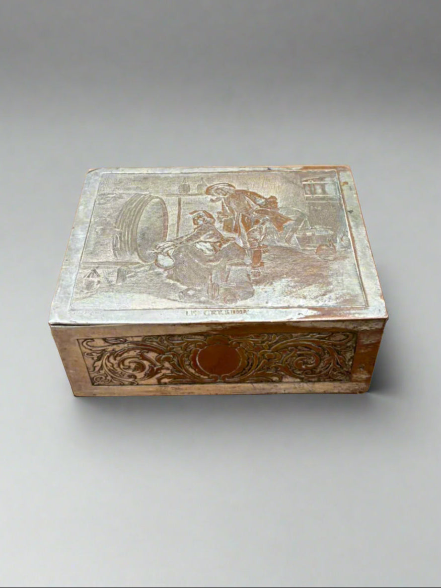 A French, silver plated on brass cigarette box with a pictorial lid depicting two figures by a wooden barrel. Circa early 1900s.