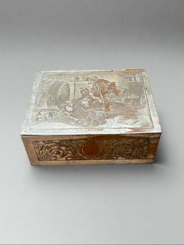 A French, silver plated on brass cigarette box with a pictorial lid depicting two figures by a wooden barrel. Circa early 1900s.