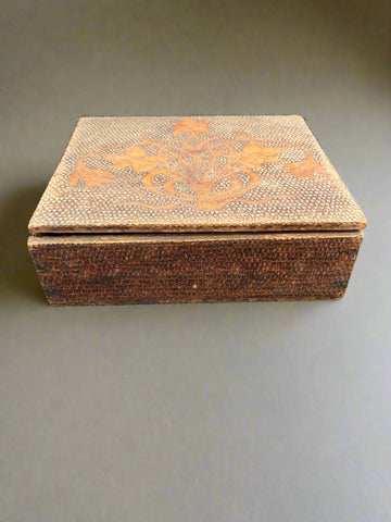 A wooden storage box with a textured surface and Art Nouveau daffodil design engraved on the lid.