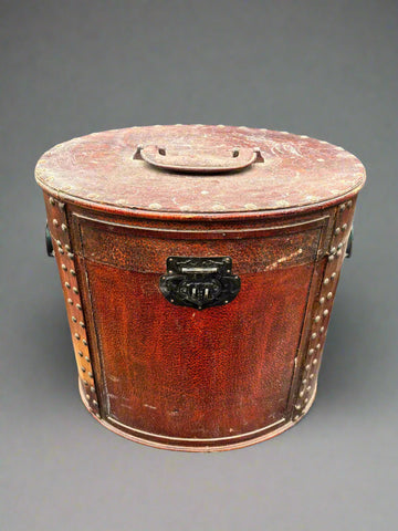 An antique, studded, round storage case with an iron clasp. It could be a hat box.