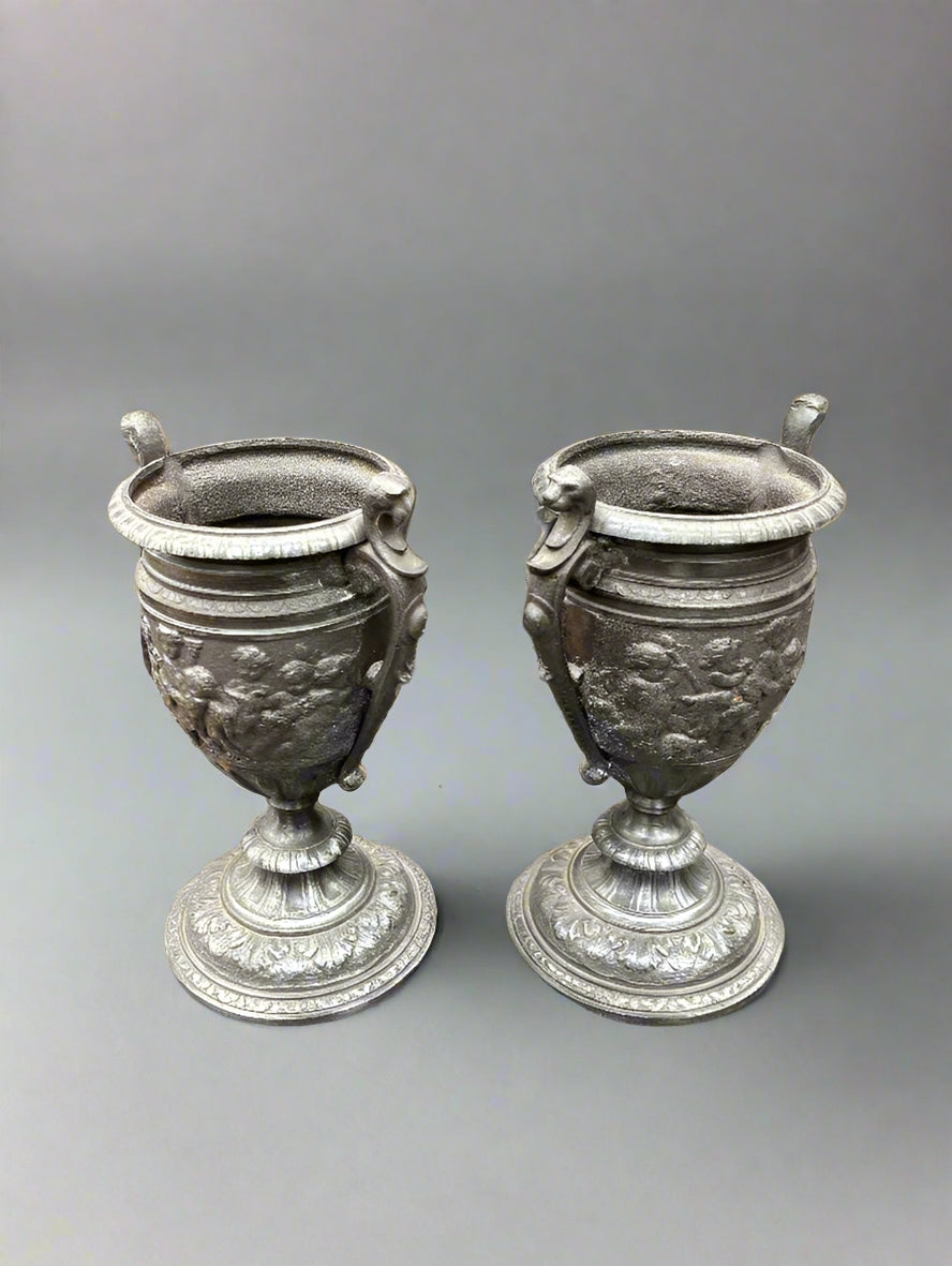 A pair of antique, neoclassical, pewter urn vases with cast cherub decoration, circa 19th century.