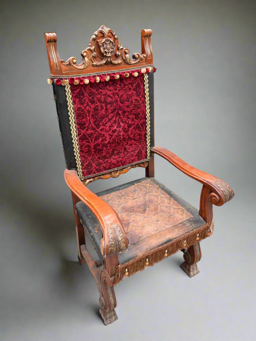 A Spanish renaissance-style throne chair with a crimson back, decorative pom poms and fringing and an embossed leather seat.