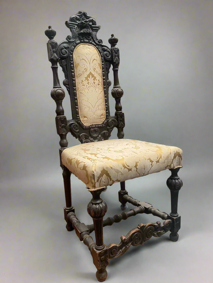 A Jacobean-revival ornately carved highback chair with cream and gold upholstery. Likely from the Victorian era.