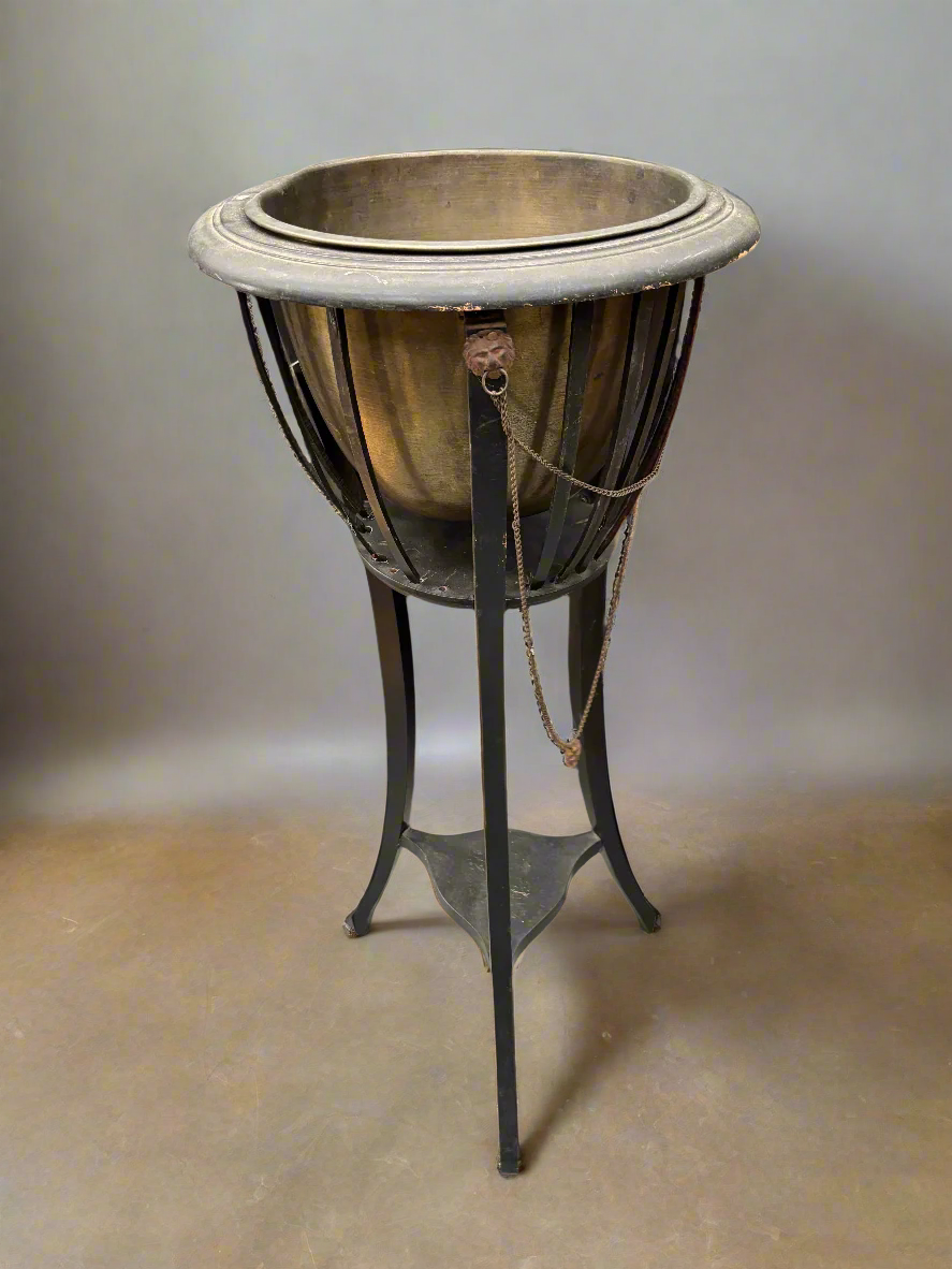 An antique brass-lined jardiniere on a tripod stand, decorated with cast metal lion heads. Circa 1910.