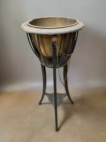 An antique brass-lined jardiniere on a tripod stand, decorated with cast metal lion heads. Circa 1910.