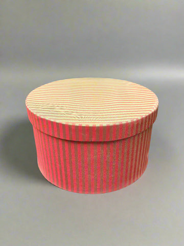 A vintage circular hat box, covered with a striped pink and green/gold fabric.