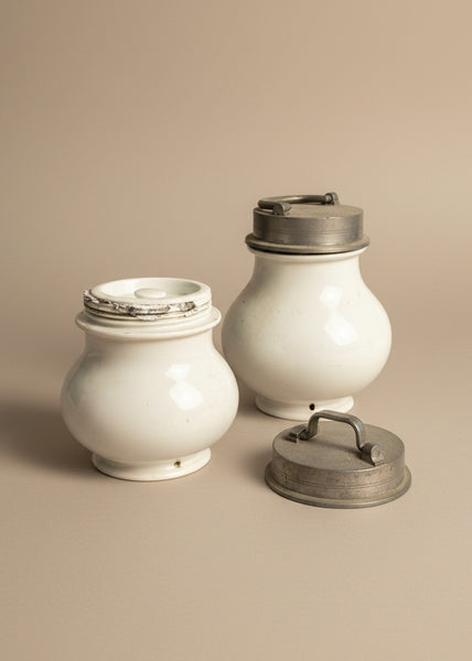 A pair of antique French bouillon soup jars with pewter lids and ironstone/ porcelain bodies, circa 19th century. The holes in the base are to hang the jars upside down in boiling water.