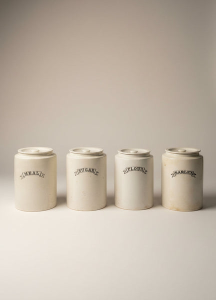 A set of vintage white ironstone kitchen storage jars with a scroll font label.