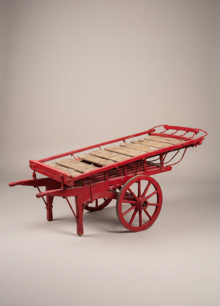 A hand-drawn costermonger's market cart, with a red painted timber frame, wooden spoked wheels and slatted deck. Circa 1900s.
