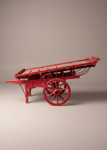 A hand-drawn costermonger's market cart, with a red painted timber frame, wooden spoked wheels and slatted deck. Circa 1900s.