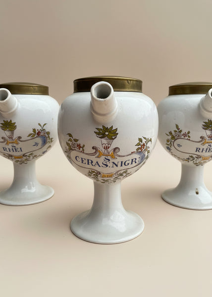A vintage pharmacist's pouring jar set, with porcelain bodies and brass lids.