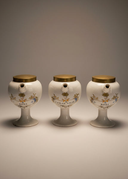 A vintage pharmacist's pouring jar set, with porcelain bodies and brass lids.