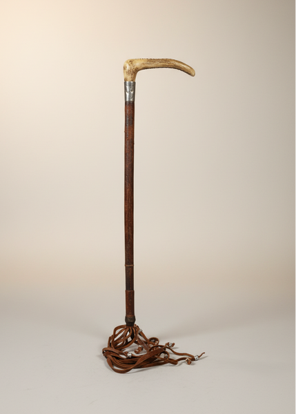 An antique hunting crop with a bone handle wrapped in a silver cuff and leather lash.