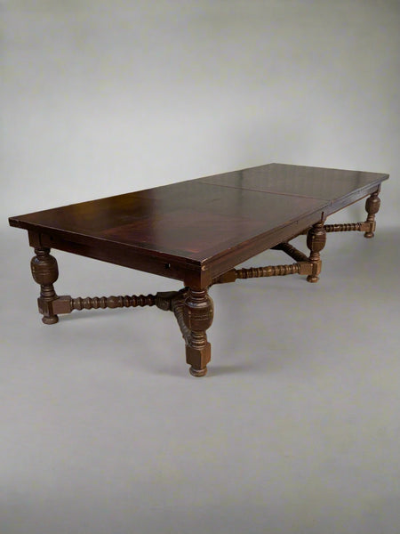 A huge, antique, rectangular, wooden dining table with heavily turned legs.