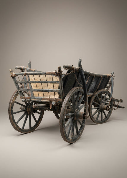 Old antique wooden farm cart with a straight gridded hinged back, suspended by a chain.