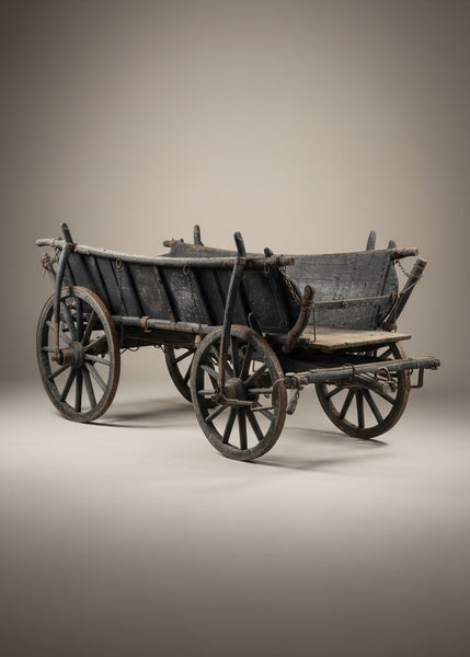 Old antique wooden farm cart with a straight gridded hinged back, suspended by a chain.