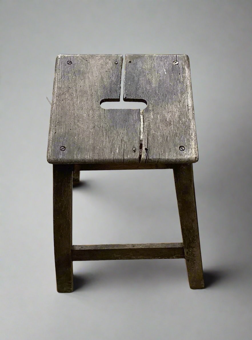 A small square wooden stool with a central hand hole in the seat.