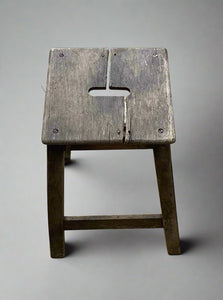 A small square wooden stool with a central hand hole in the seat.