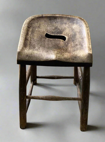 Small curved wooden stool with a carry hand hole in the seat and footrest.