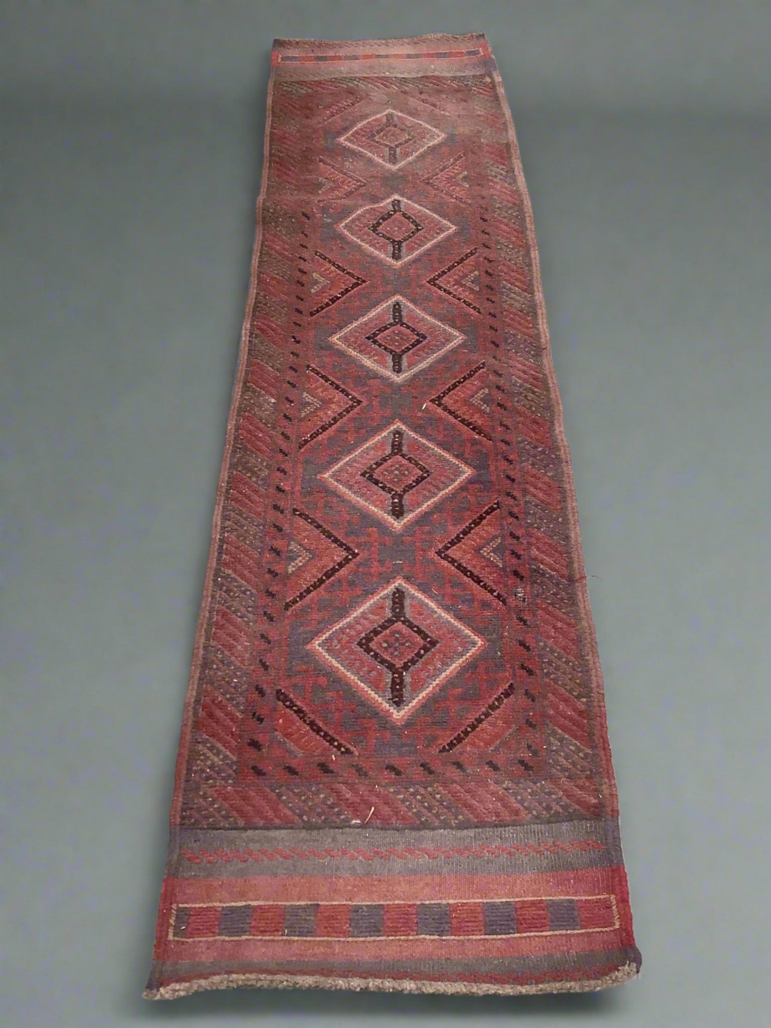 Long red rug woven with red and grey thread in geometric patterns.