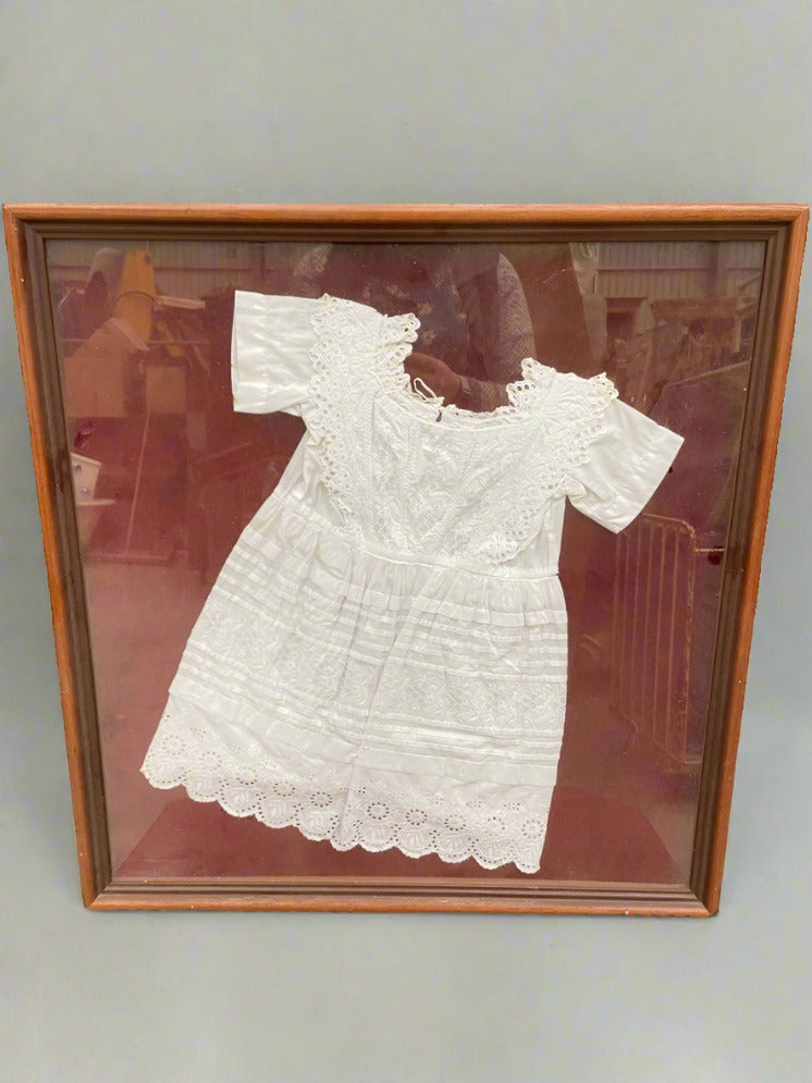 White Victorian-style lacy child's dress in a square wooden frame.