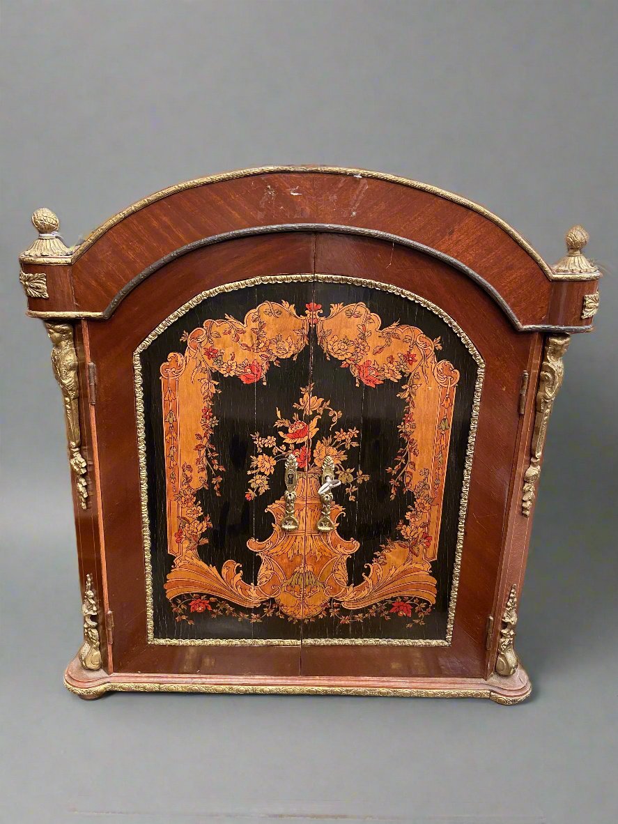 Small double-door marquetry cabinet with an inlaid floral design and golden finishes.