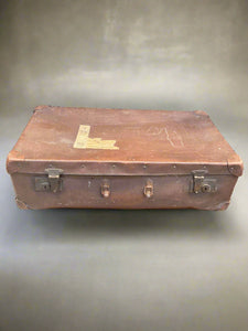 Brown studded suitcase with a newspaper clipping attached on top.