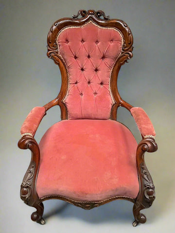 Antique salmon pink buttoned armchair with an ornately carved frame and padded armrests, standing on cabriole legs.