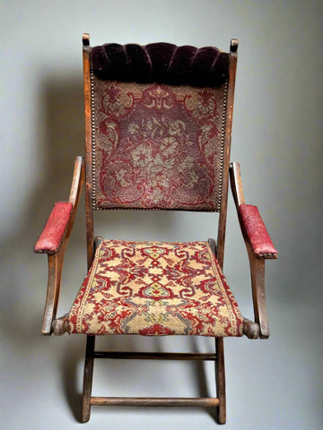 Eclectic fold-up tapestry chair with a wooden frame padded purple velvet headrest and studded leather armrests.