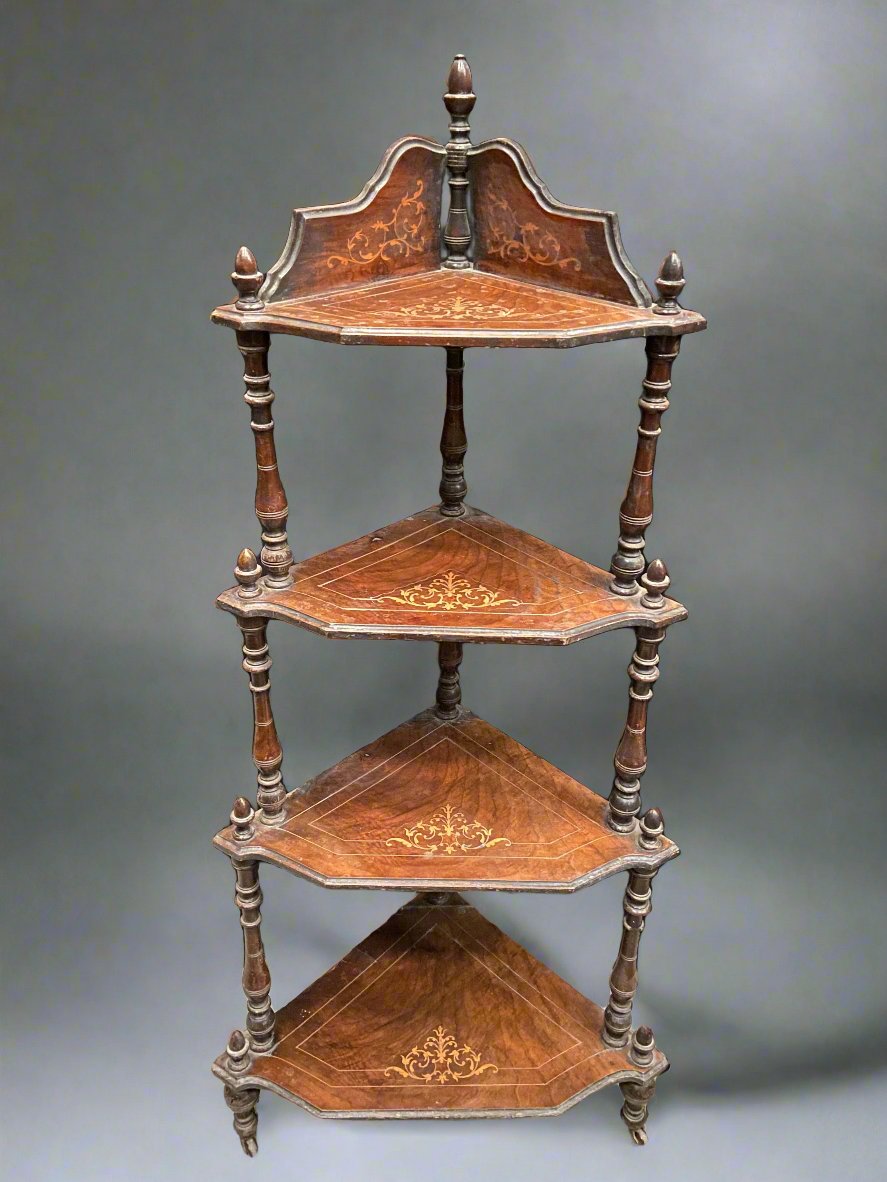 Four shelved wooden display corner unit with an ornate inlaid design and three finials. The unit is on castors.