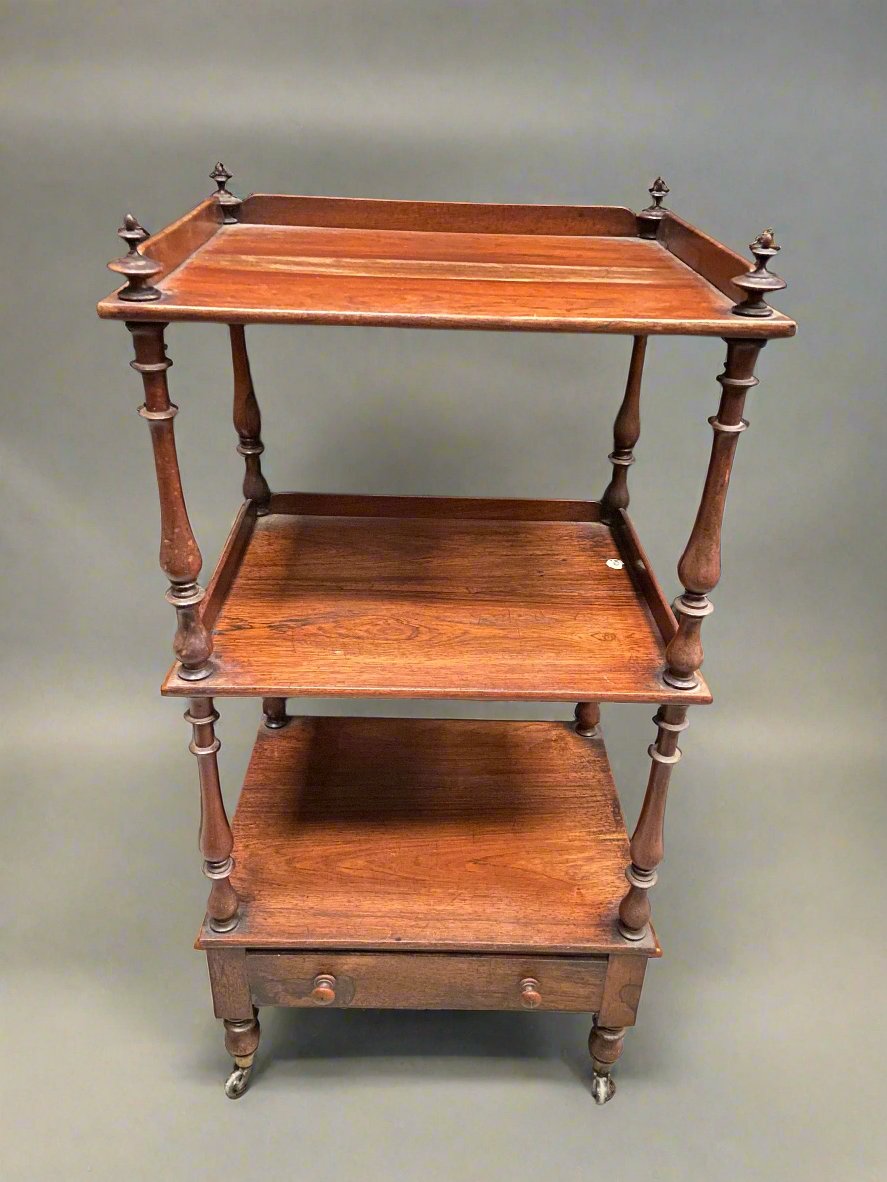 Square wooden three-tier display unit with a single drawer and finials. The unit sits on castors.