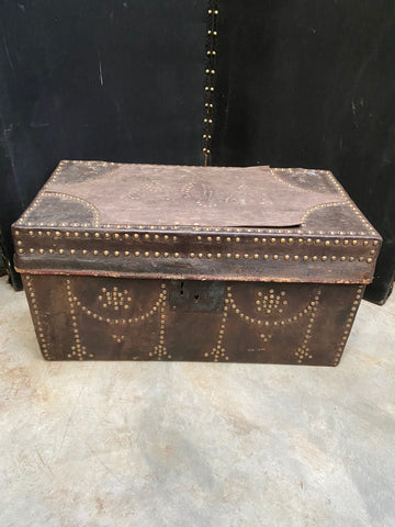 Large dark brown leather stagecoach trunk decorated with round brass studs. The top of the trunk shows the faint initials AQA.