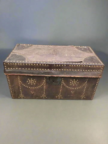 Large dark brown leather stagecoach trunk decorated with round brass studs. The top of the trunk shows the faint initials AQA.