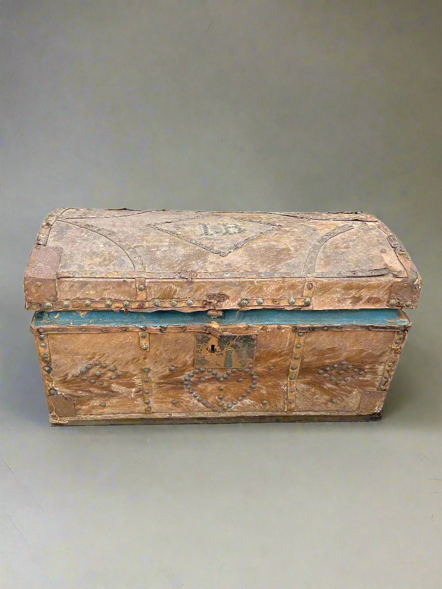 Hide covered dome top storage trunk with heart and diamond-shaped tack decorations. The trunk is initialled with the letters I.B.