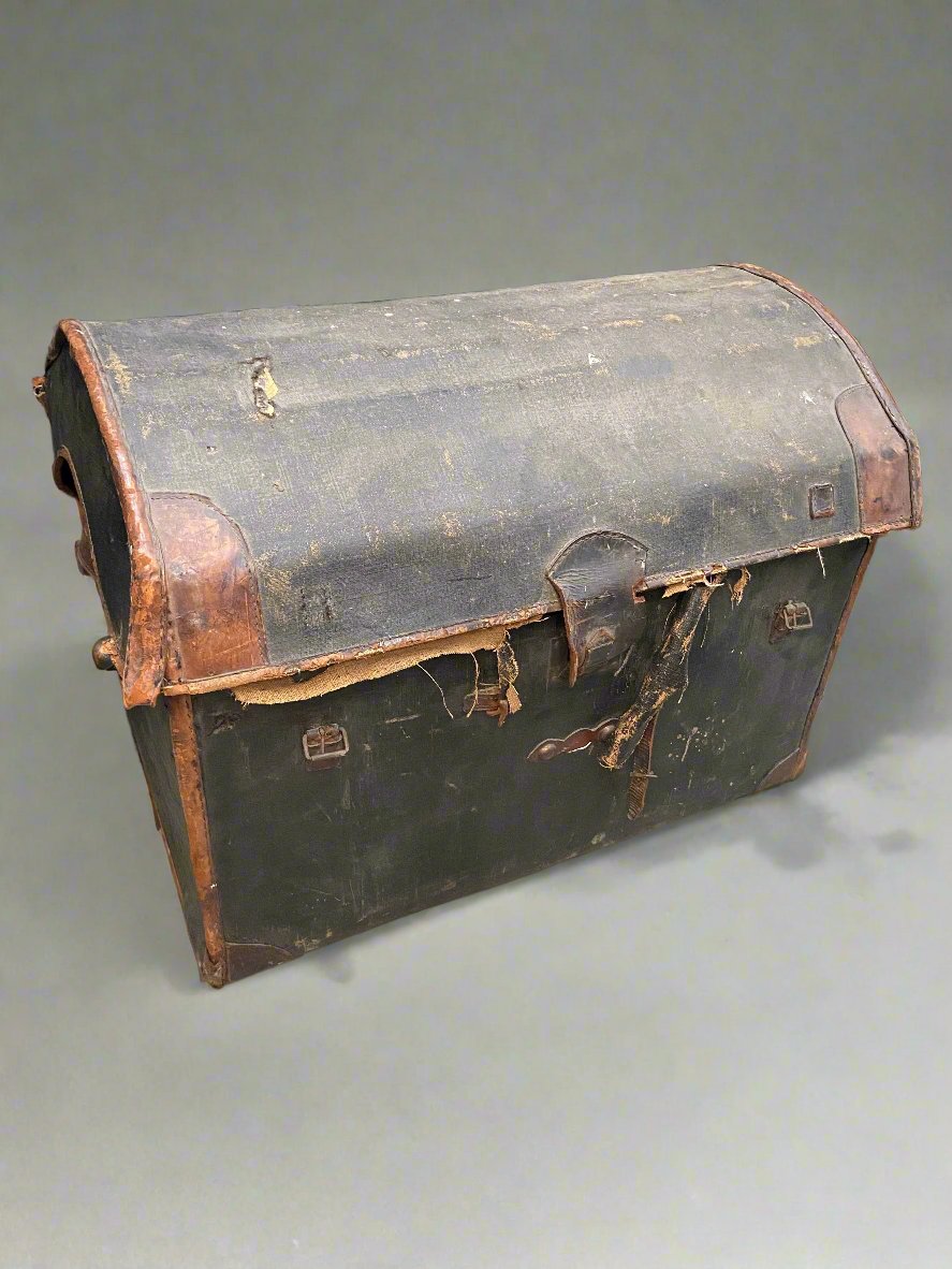 Black and brown dome-topped leather storage chest with a buckled close.