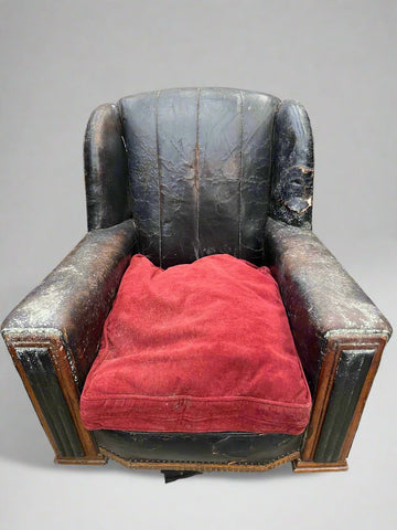 Heavily aged Art Deco dark leather chair with a red seat cushion.