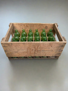 18 vintage green glass bottles sitting inside a wooden crate stamped with German writing.