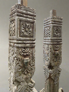 A pair of tall carved decorative columns with an ornate cross-shaped base and top.