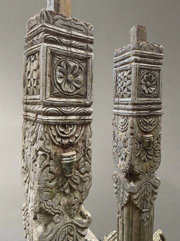 A pair of tall carved decorative columns with an ornate cross-shaped base and top.