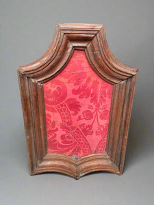 Symmetrical curved wooden picture frame lined with floral red silk fabric.