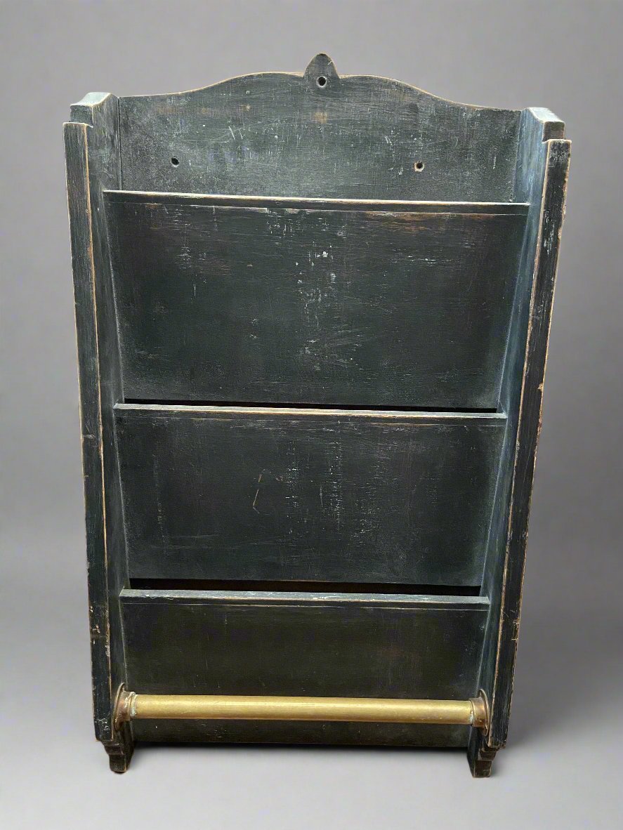 Black magazine rack with a brass bar. Circa 1895.

You would often see these in barbershops and coffee houses, with the brass bar holding a rag for a barman or newspapers.