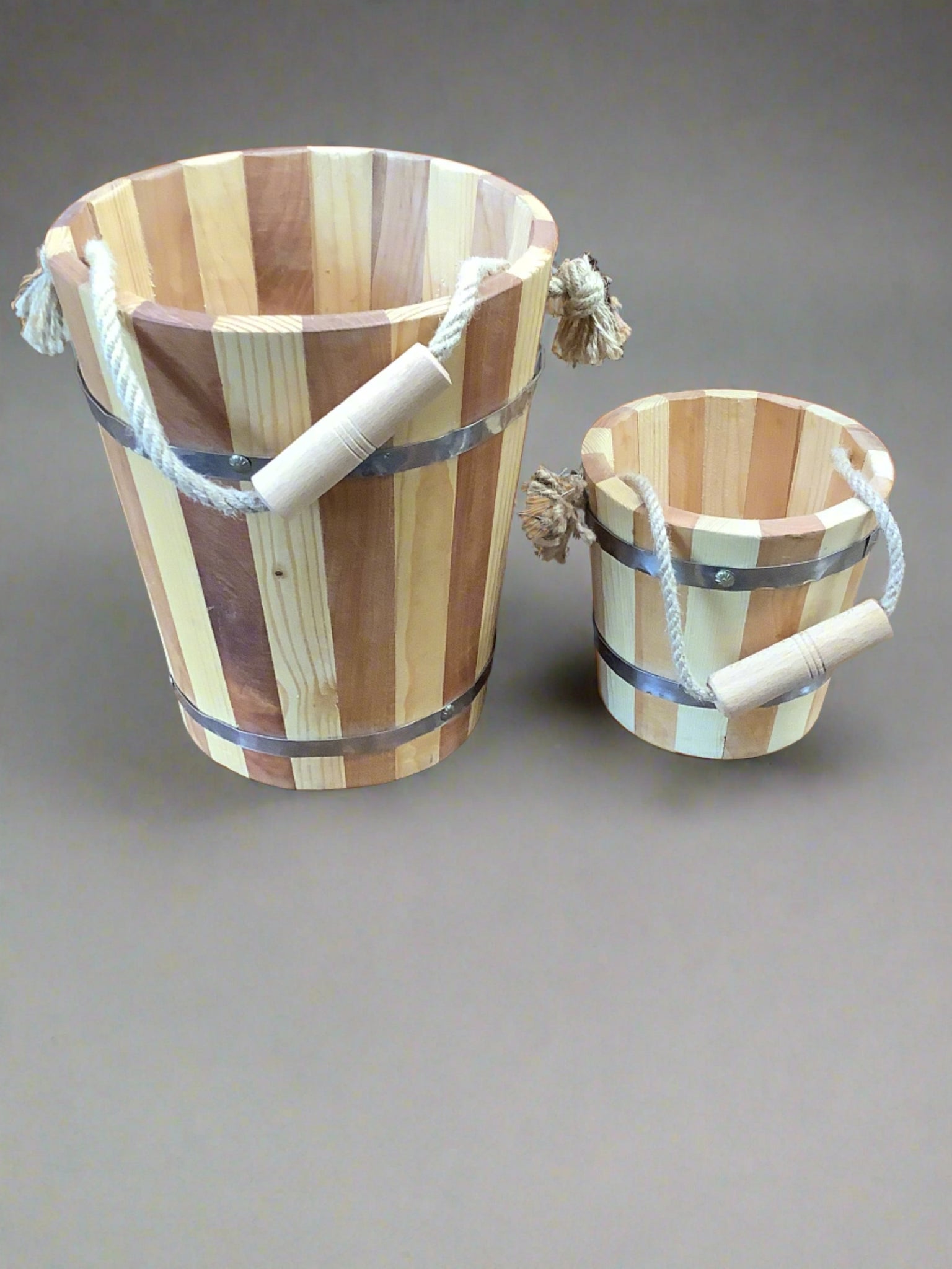 A pair of wooden two-tone stripy buckets with a rope handle and metal banding.