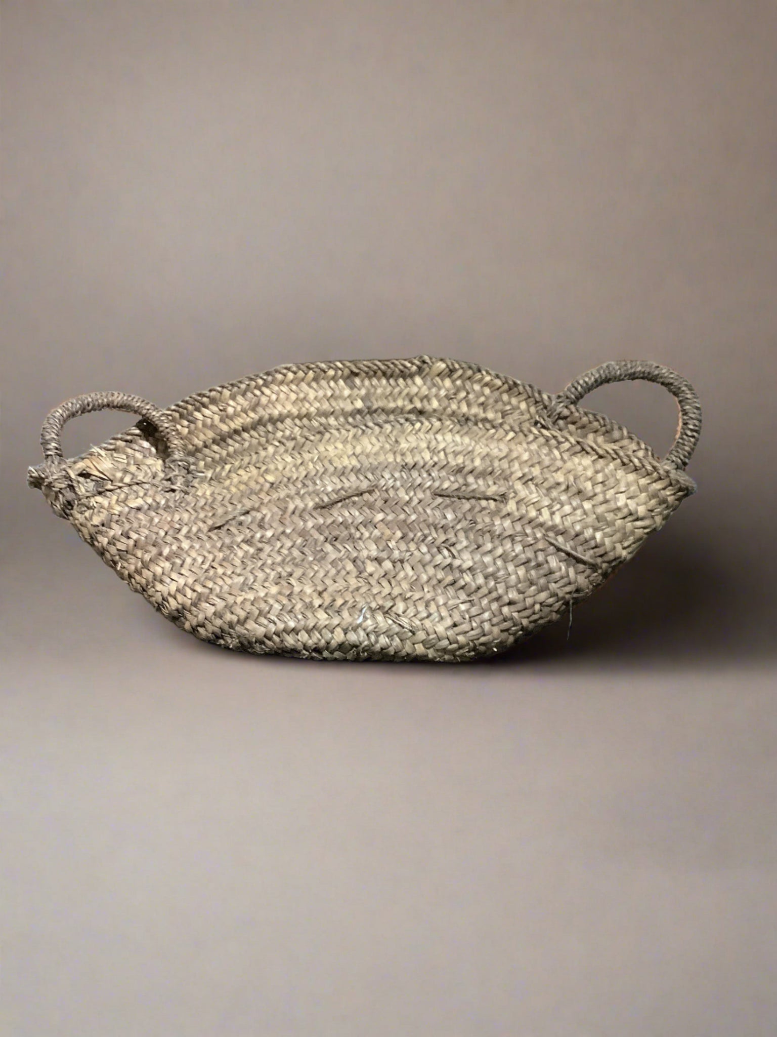 Low basket with twin handles woven from palm leaves.