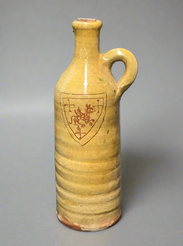 Tall and cylindrical yellow earthenware jug with decorative coat of arms s'graffito detailing, gloss glazing and handle.