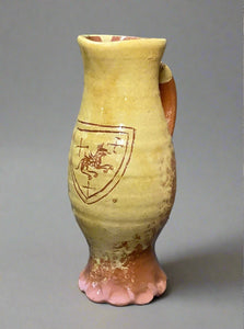 Tall yellow earthenware jug with a decorative coat of arms s'graffito detailing, fluted base, gloss glazing and handle.