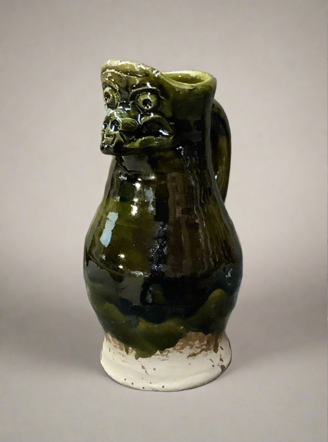 Green earthenware jug with decorative gargoyle moulding, fluted lip, gloss glazing and handle.