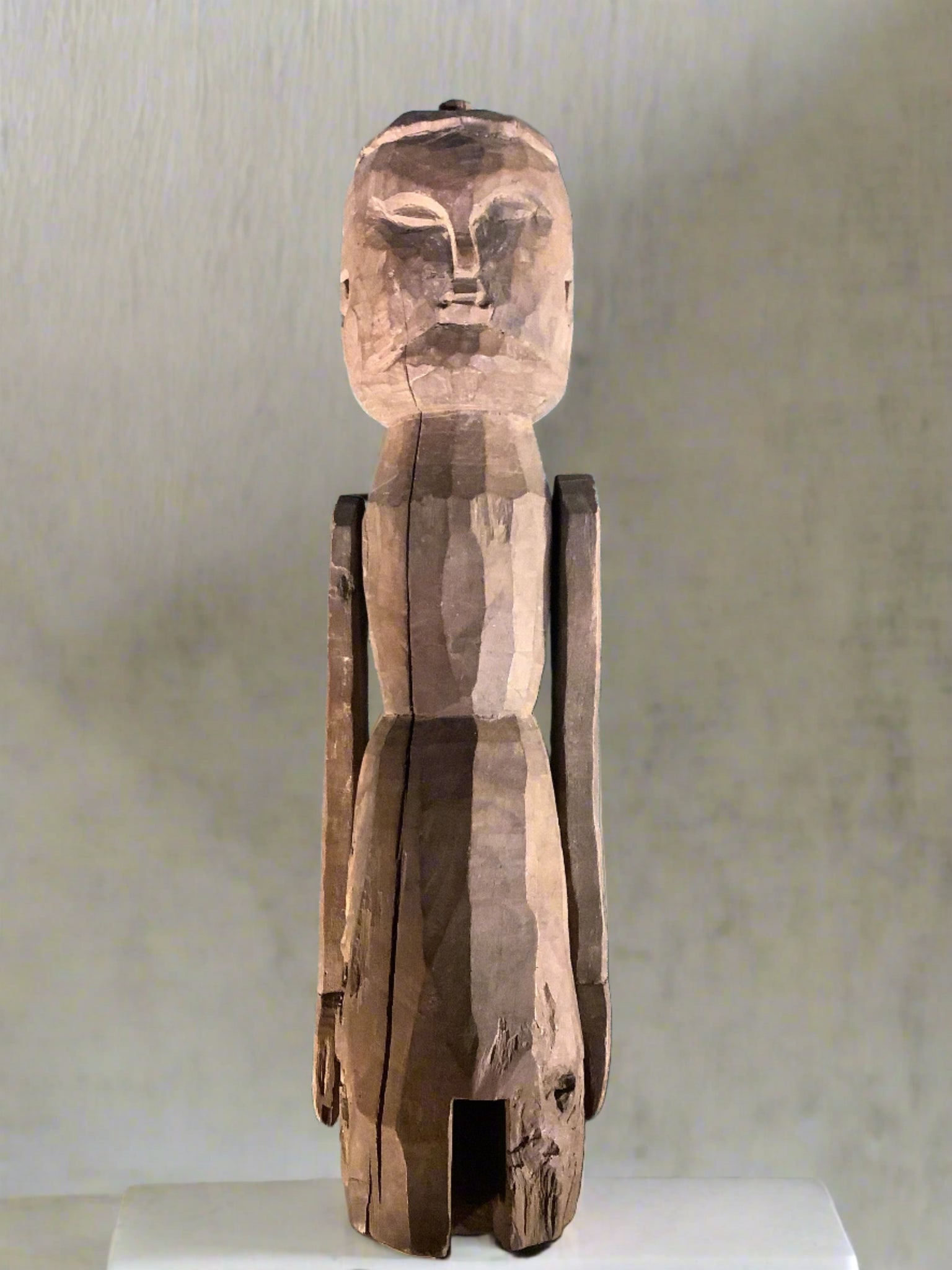 Hand-carved sculpture of a man in primitive style with elongated limbs and stylised features.